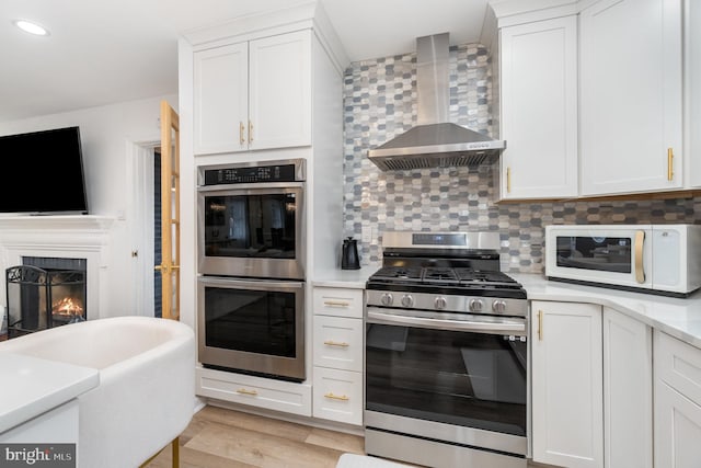 kitchen with wall chimney exhaust hood, white cabinets, appliances with stainless steel finishes, and decorative backsplash