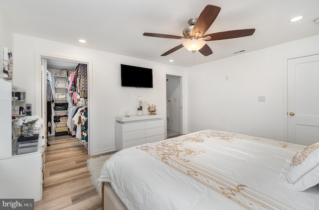 bedroom featuring ceiling fan, a closet, a walk in closet, and light wood-type flooring