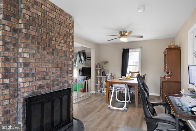 office area with ceiling fan, light hardwood / wood-style flooring, and a brick fireplace