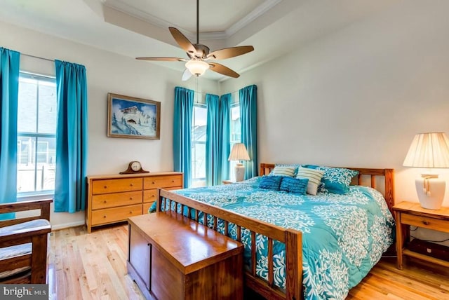 bedroom featuring a tray ceiling, multiple windows, and light wood-type flooring