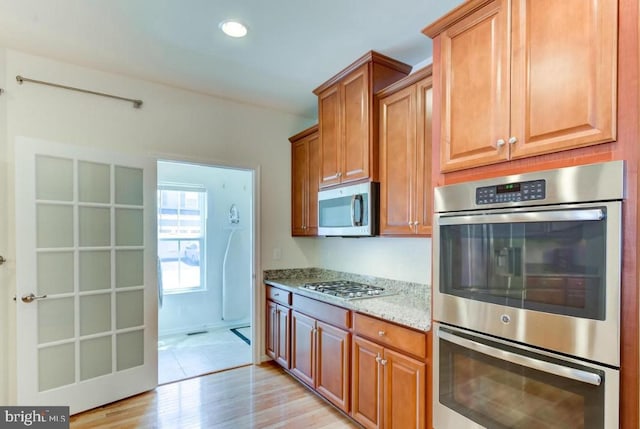 kitchen with light stone counters, appliances with stainless steel finishes, and light wood-type flooring