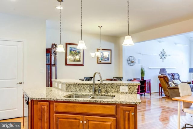 kitchen with a center island with sink, sink, pendant lighting, and light stone counters