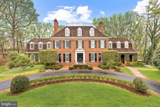 colonial inspired home with aphalt driveway, a front yard, brick siding, and a chimney