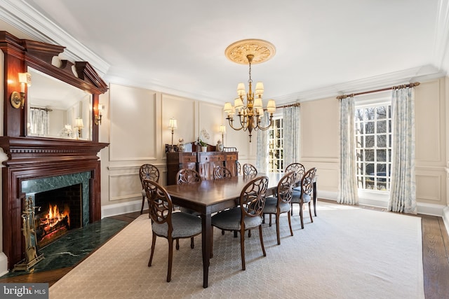 dining space with crown molding, a decorative wall, a premium fireplace, wood finished floors, and a chandelier