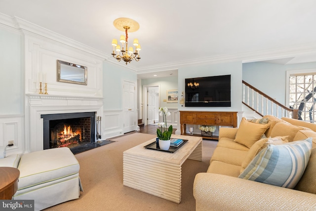 carpeted living room with wainscoting, a fireplace with flush hearth, an inviting chandelier, crown molding, and a decorative wall