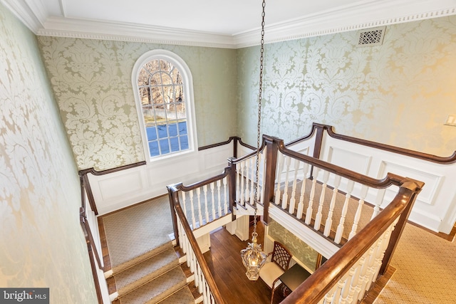 staircase with ornamental molding, a wainscoted wall, visible vents, and wallpapered walls