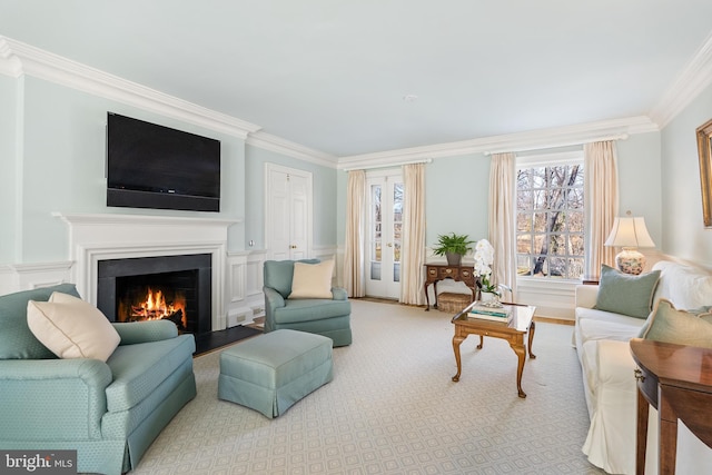 living area featuring a lit fireplace, ornamental molding, and wainscoting