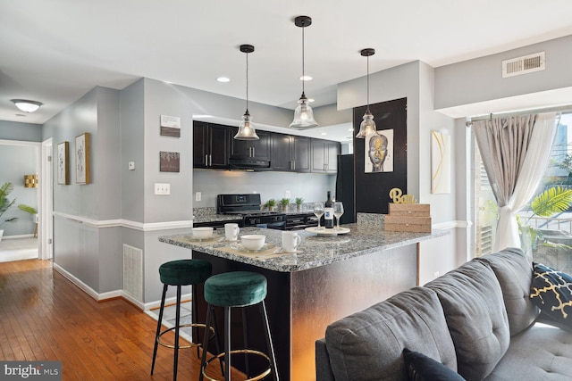 kitchen with kitchen peninsula, a kitchen breakfast bar, light stone countertops, black range with gas cooktop, and range hood