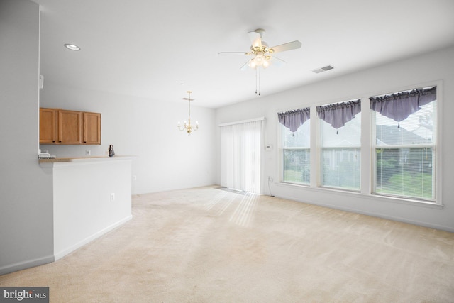 carpeted spare room featuring ceiling fan with notable chandelier