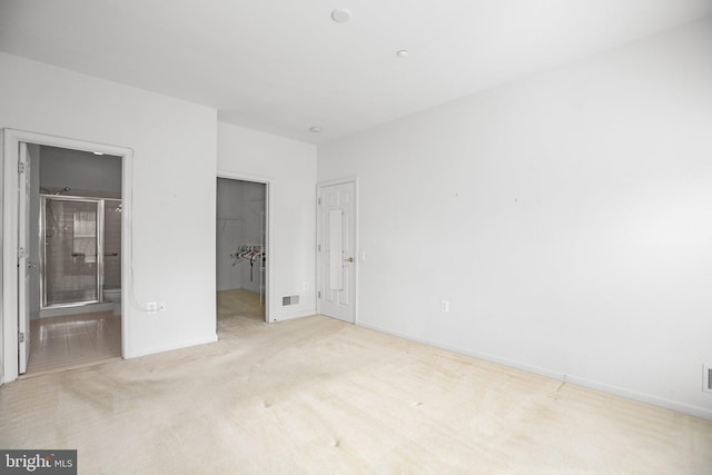 unfurnished bedroom with a closet, light colored carpet, and ensuite bath