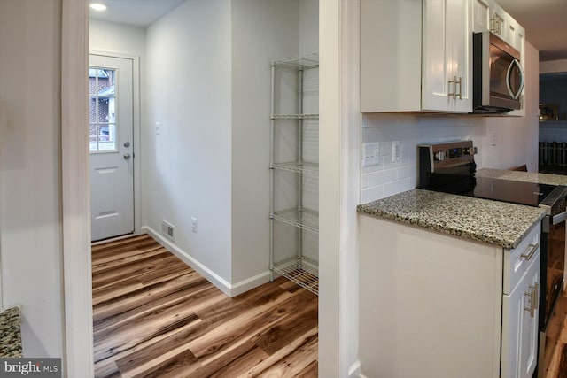 kitchen with stainless steel appliances, light stone counters, light hardwood / wood-style floors, white cabinets, and decorative backsplash