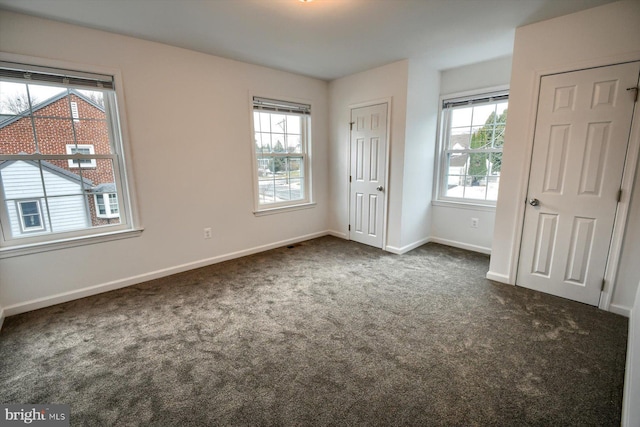 unfurnished bedroom featuring multiple closets, dark carpet, and multiple windows