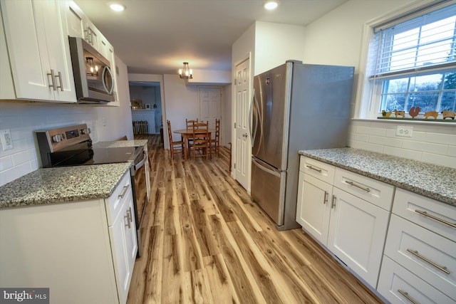 kitchen with white cabinetry, tasteful backsplash, light stone counters, light hardwood / wood-style flooring, and appliances with stainless steel finishes