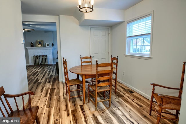 dining room featuring wood-type flooring, a brick fireplace, and ceiling fan