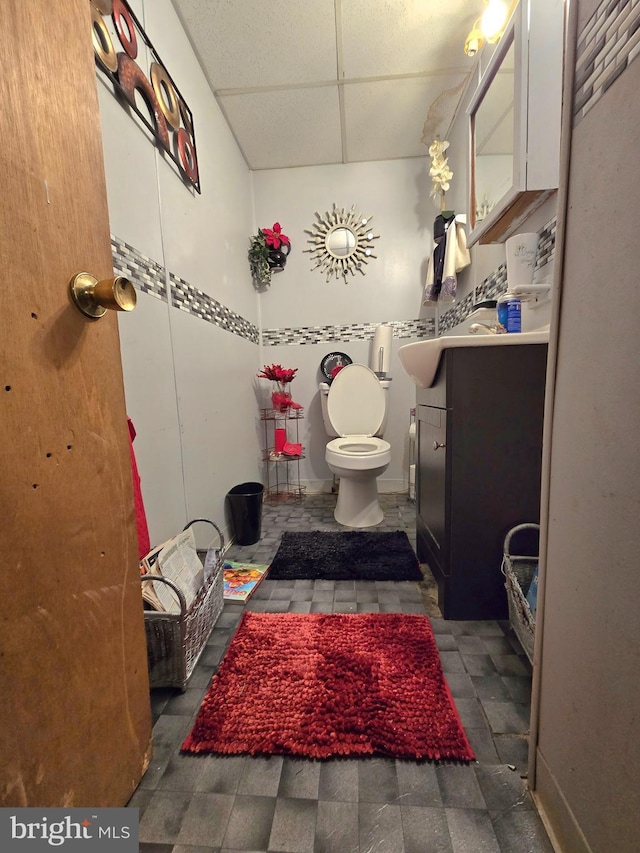 bathroom with a drop ceiling, toilet, and vanity