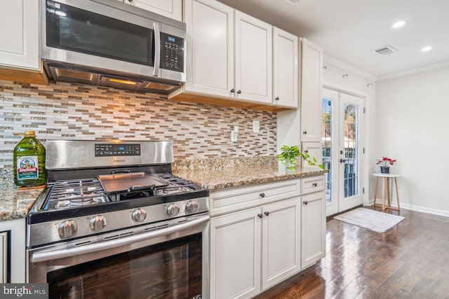 kitchen with light stone countertops, appliances with stainless steel finishes, white cabinetry, tasteful backsplash, and crown molding