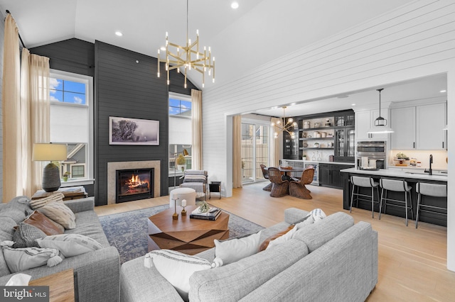 living room featuring an inviting chandelier, a fireplace, high vaulted ceiling, and light wood-type flooring