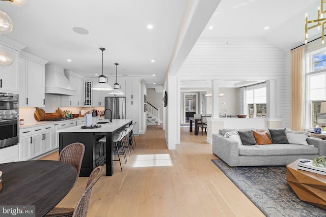 living room featuring lofted ceiling, sink, and light hardwood / wood-style floors