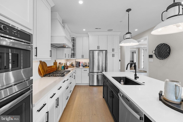 kitchen with appliances with stainless steel finishes, pendant lighting, white cabinetry, sink, and custom exhaust hood