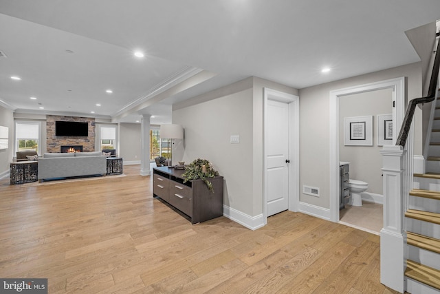 interior space with ornate columns, a stone fireplace, crown molding, and light wood-type flooring