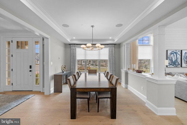 dining space featuring crown molding, a raised ceiling, an inviting chandelier, and light wood-type flooring