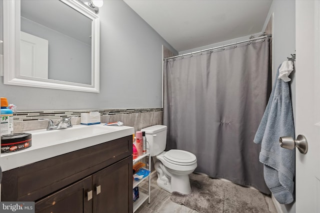 bathroom with toilet, a shower with shower curtain, vanity, tile walls, and wainscoting