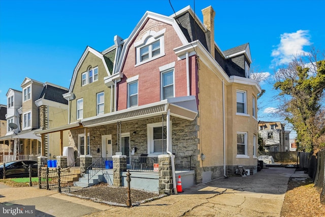 townhome / multi-family property with covered porch, stone siding, a residential view, and a gambrel roof