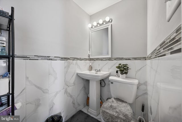 half bath featuring toilet, tile walls, and a sink