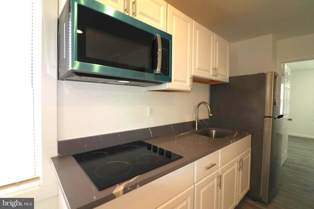 kitchen with white cabinetry, sink, black electric cooktop, and dark stone counters