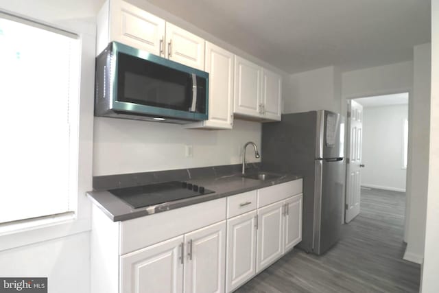 kitchen with sink, stainless steel fridge, white cabinetry, black electric cooktop, and dark hardwood / wood-style flooring