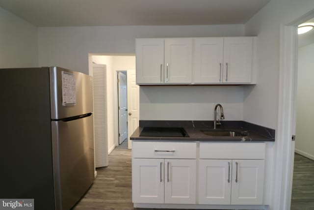 kitchen featuring black electric stovetop, sink, stainless steel refrigerator, and white cabinets