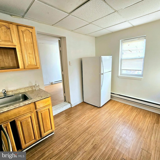 kitchen with light wood-type flooring, white fridge, a baseboard radiator, and sink