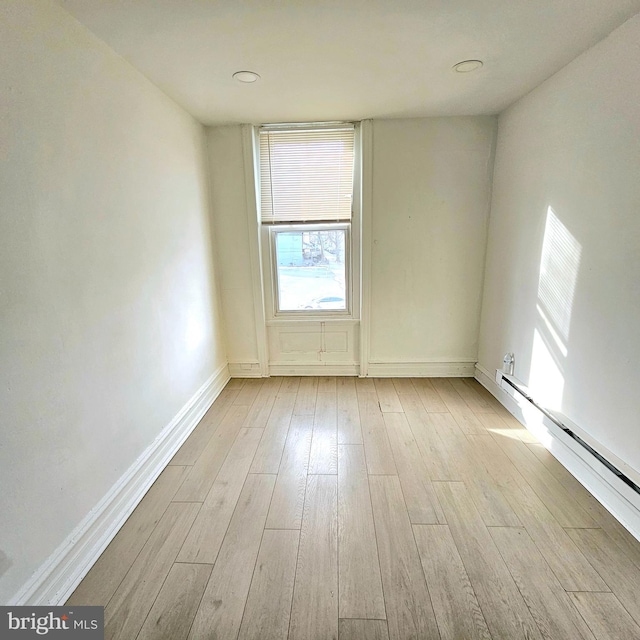 unfurnished room featuring a baseboard radiator and light hardwood / wood-style flooring