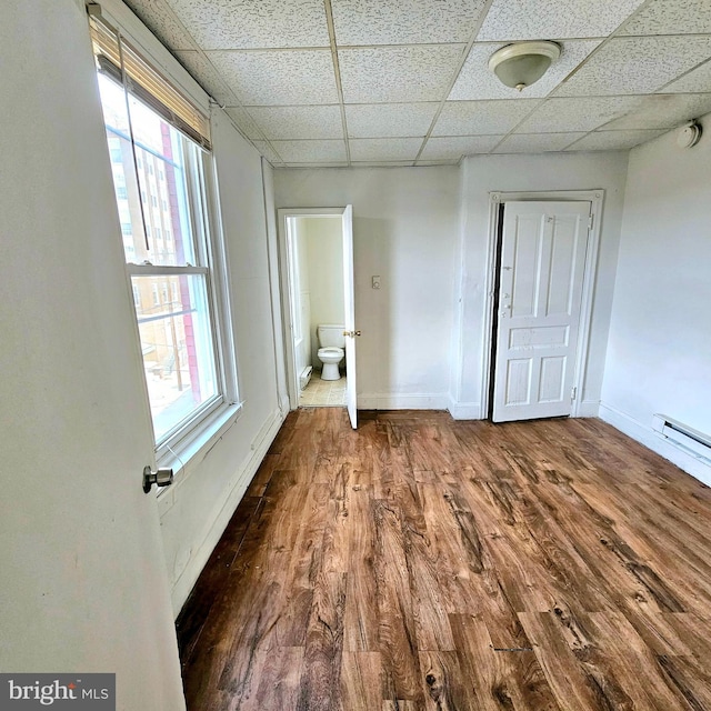 interior space featuring a paneled ceiling, hardwood / wood-style flooring, a baseboard radiator, and a healthy amount of sunlight