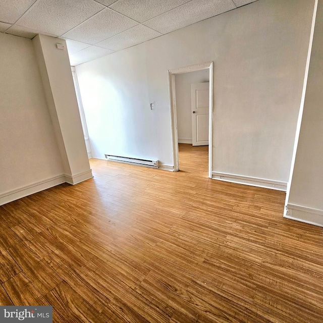 unfurnished room featuring baseboard heating, light hardwood / wood-style flooring, and a drop ceiling