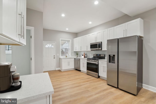 kitchen with appliances with stainless steel finishes, light hardwood / wood-style flooring, white cabinetry, and sink