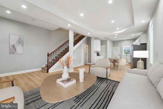 living room featuring a tray ceiling, sink, and light wood-type flooring