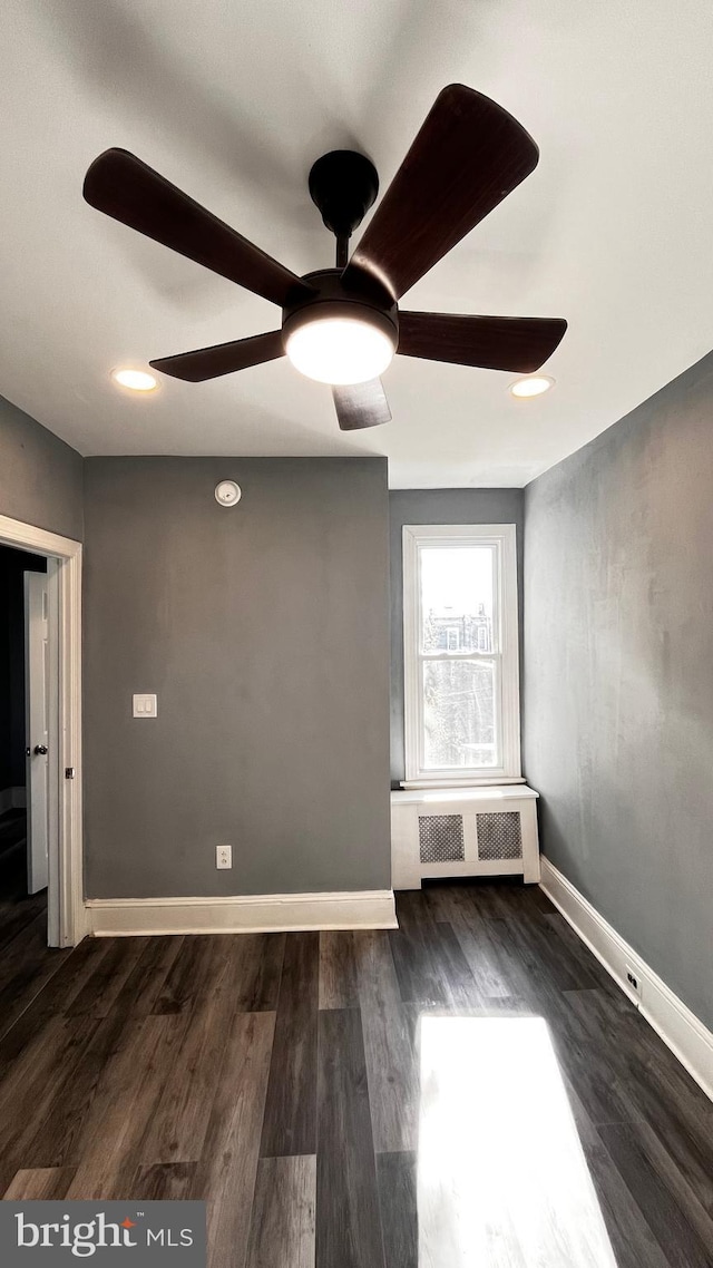 unfurnished room featuring ceiling fan, radiator heating unit, and dark wood-type flooring