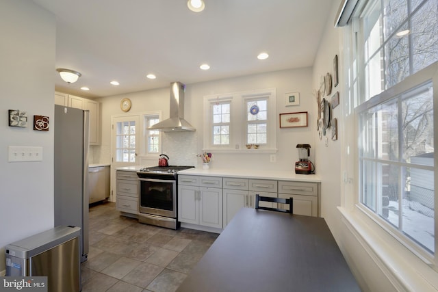 kitchen featuring appliances with stainless steel finishes, a wealth of natural light, wall chimney range hood, and backsplash