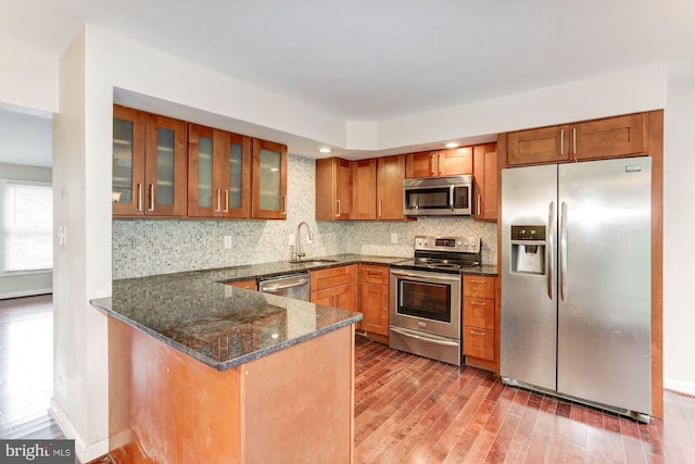 kitchen with kitchen peninsula, backsplash, stainless steel appliances, and dark stone countertops