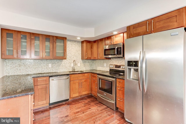 kitchen featuring sink, backsplash, dark stone countertops, hardwood / wood-style floors, and appliances with stainless steel finishes