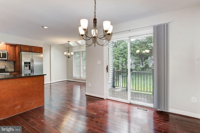 kitchen with dark wood-type flooring, hanging light fixtures, an inviting chandelier, backsplash, and appliances with stainless steel finishes