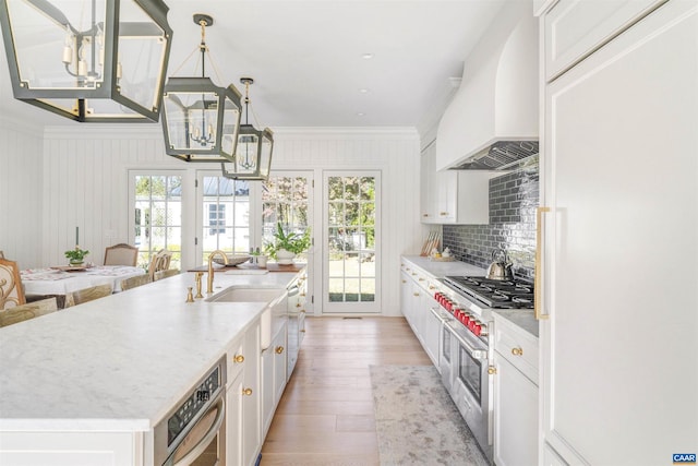 kitchen with a wealth of natural light, pendant lighting, white cabinets, an island with sink, and custom range hood