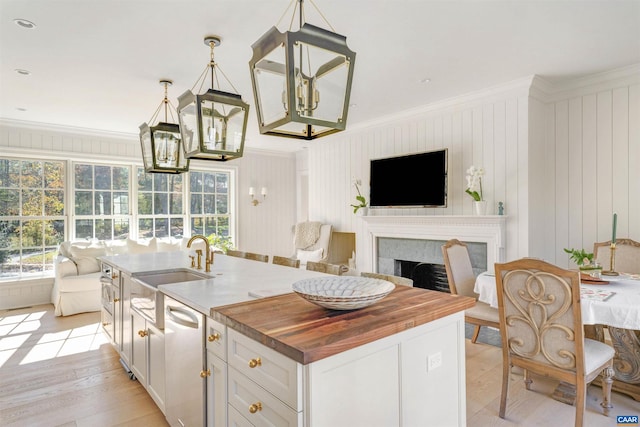 kitchen featuring ornamental molding, light hardwood / wood-style floors, hanging light fixtures, and an island with sink