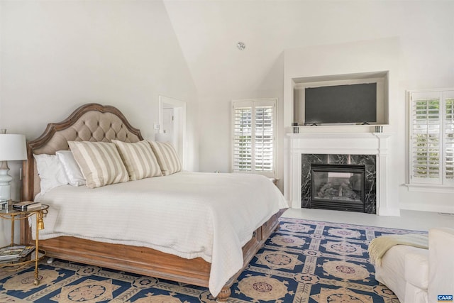 bedroom featuring high vaulted ceiling, a premium fireplace, and multiple windows