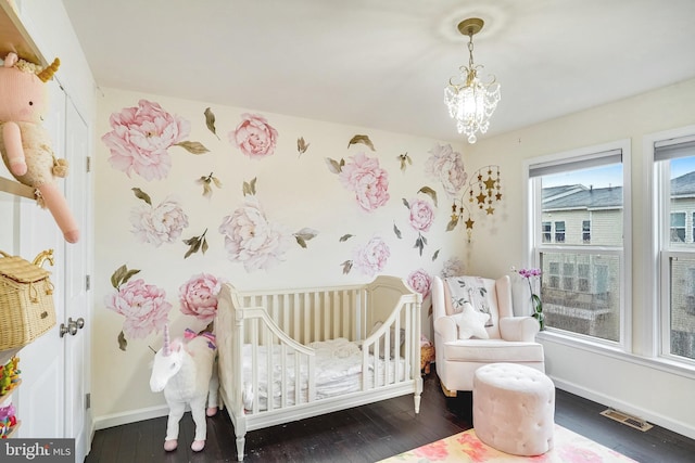 bedroom with a crib, baseboards, visible vents, dark wood-style floors, and a chandelier