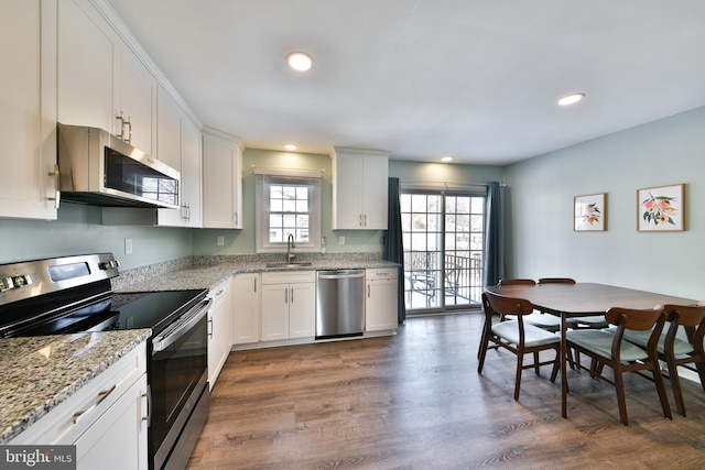 kitchen with appliances with stainless steel finishes, sink, white cabinetry, light stone countertops, and dark hardwood / wood-style floors