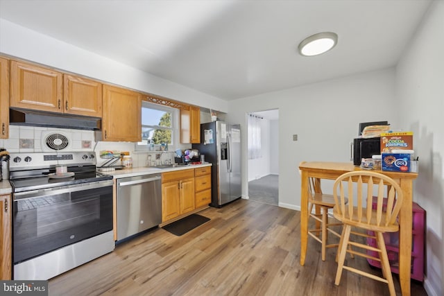 kitchen with stainless steel appliances, sink, tasteful backsplash, and light wood-type flooring