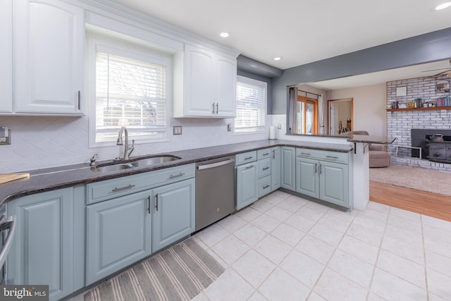 kitchen featuring kitchen peninsula, stainless steel dishwasher, a wood stove, white cabinets, and sink