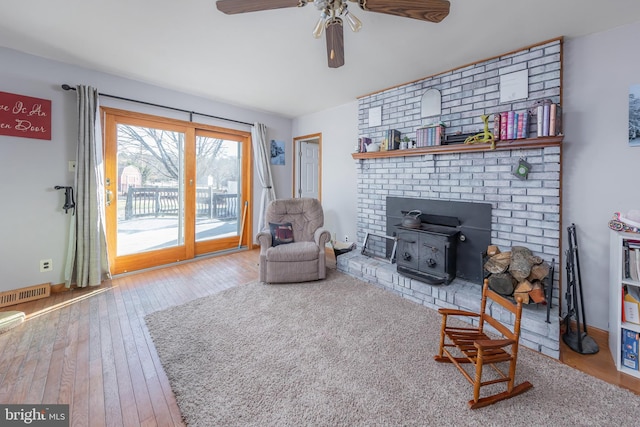 living room featuring ceiling fan, a wood stove, and light hardwood / wood-style flooring